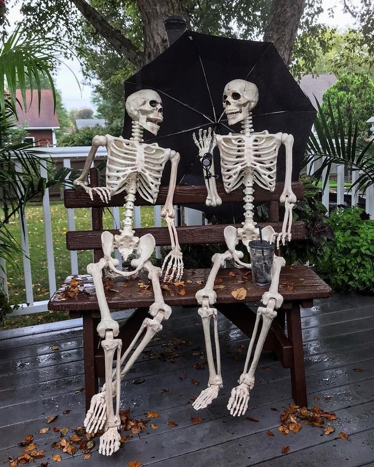 two skeletons sitting on a bench with an umbrella