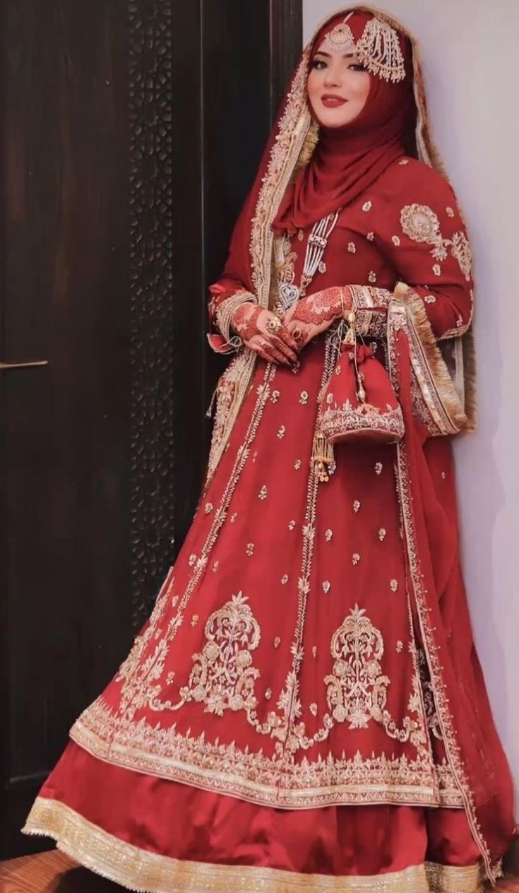 a woman in a red and gold bridal gown standing against a wall with her hands on her hips