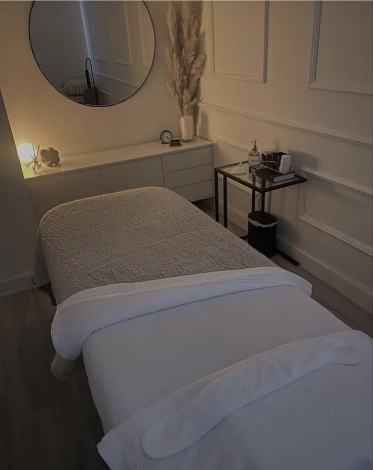 a white bed sitting in a bedroom next to a mirror and table with a lamp on it