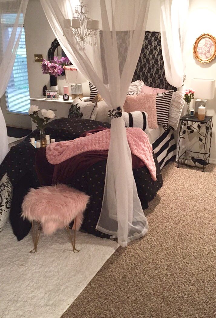 a white canopy bed sitting in a bedroom next to a pink ottoman and table with flowers on it