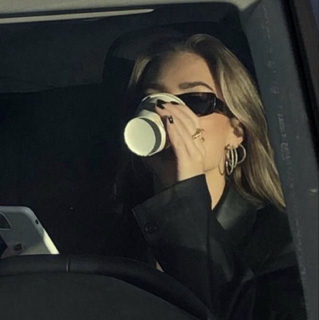 a woman drinking from a cup while sitting in a car