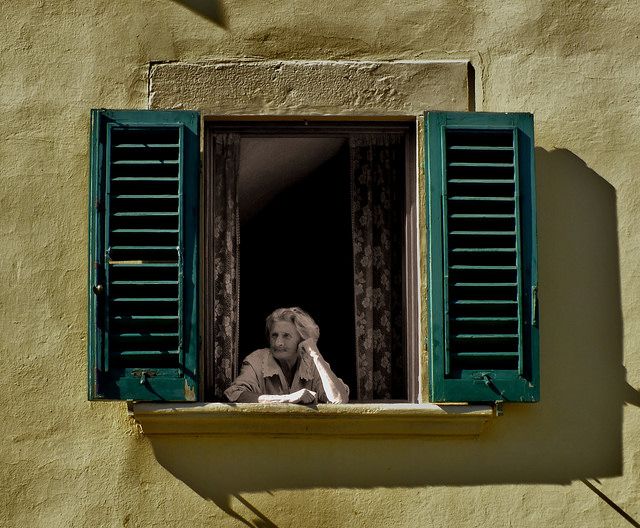 a woman is looking out the window with green shutters