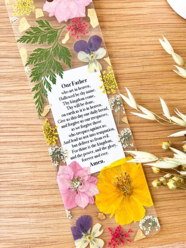 a bookmark with flowers and a poem on it sitting next to some dried grass