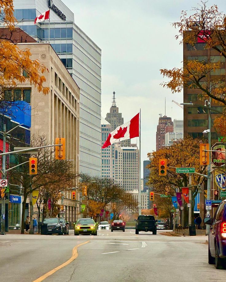 the canadian flag is flying high in the sky above the city street with cars driving down it