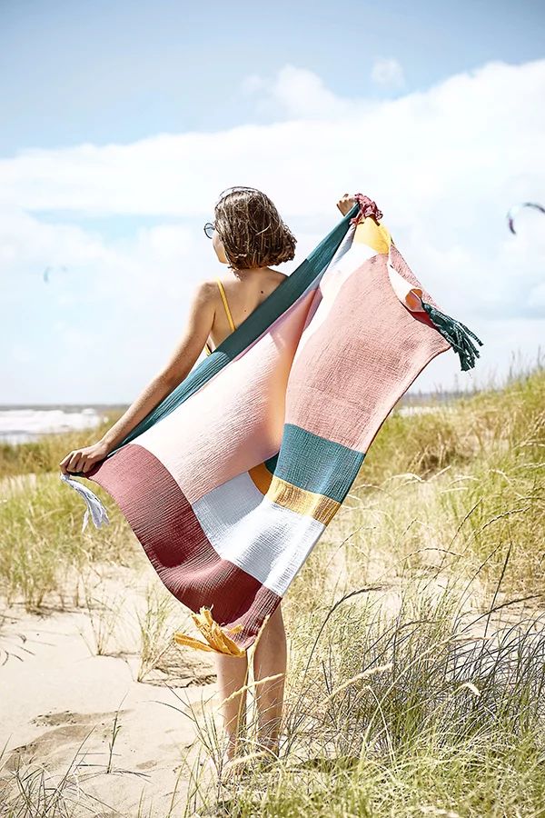 a woman standing on the beach holding a blanket