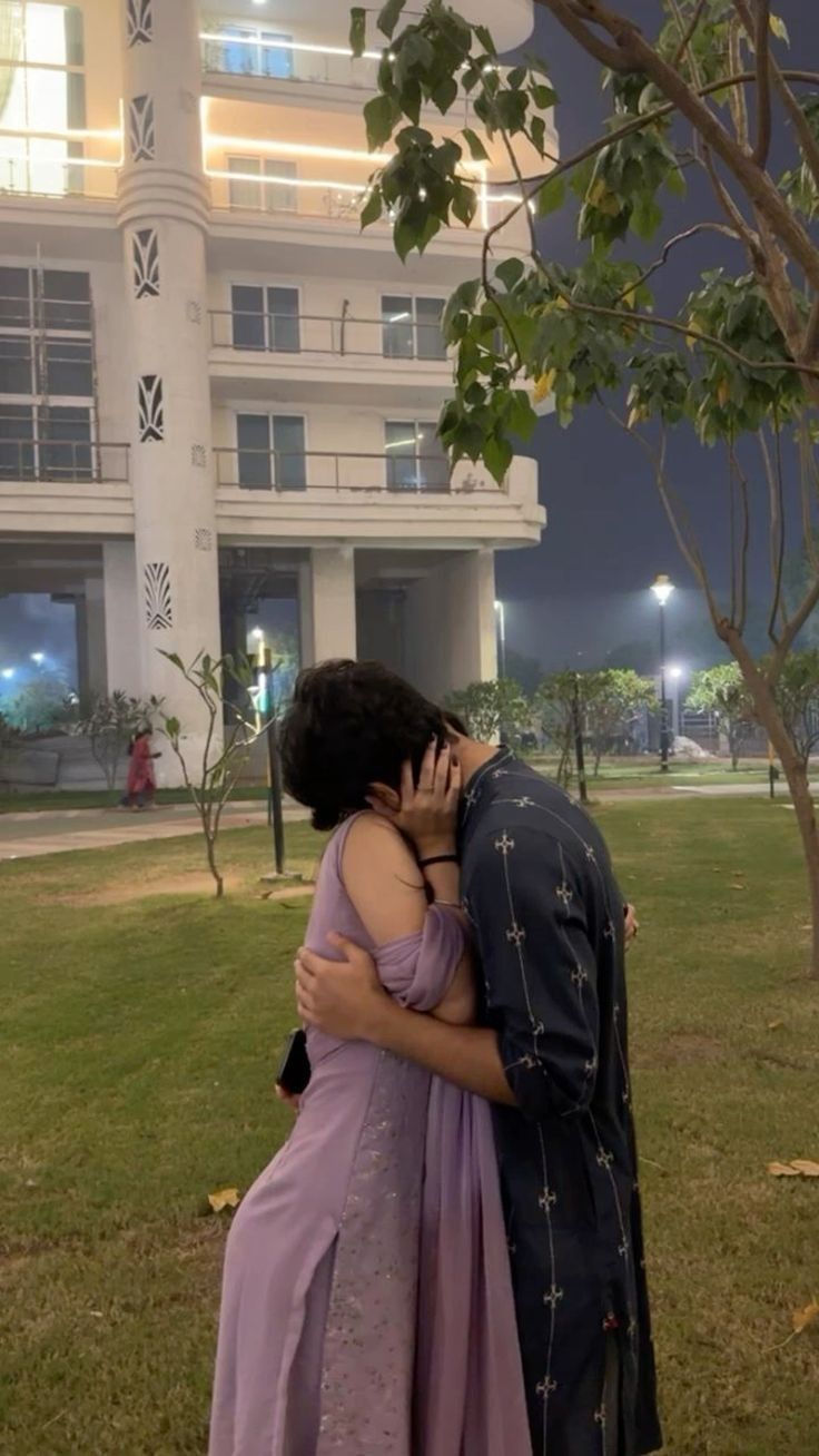 a man and woman embracing each other in front of a large white building at night