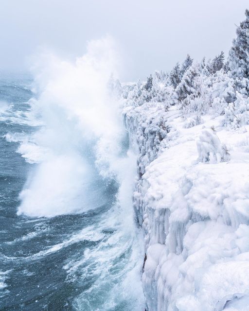 an ocean cliff is covered in ice and snow as it breaks into the water below