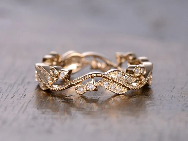 a gold wedding band with leaves and diamonds on the side, sitting on a wooden surface