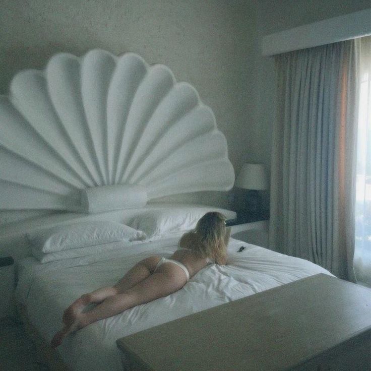 a woman laying on top of a bed next to a large white shell headboard