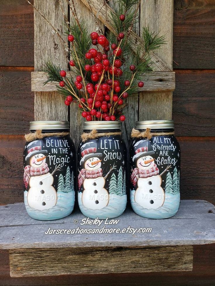 three mason jars with snowmen painted on them sitting next to berries and pine cones