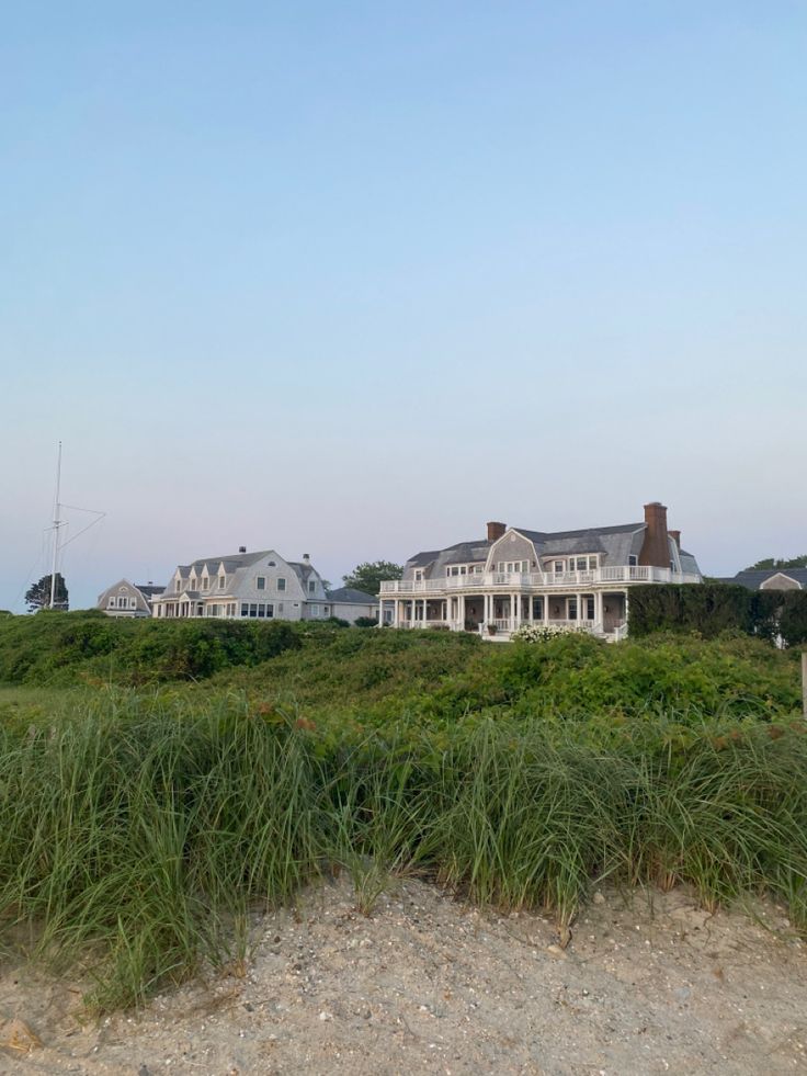 a large white house sitting on top of a lush green field next to tall grass