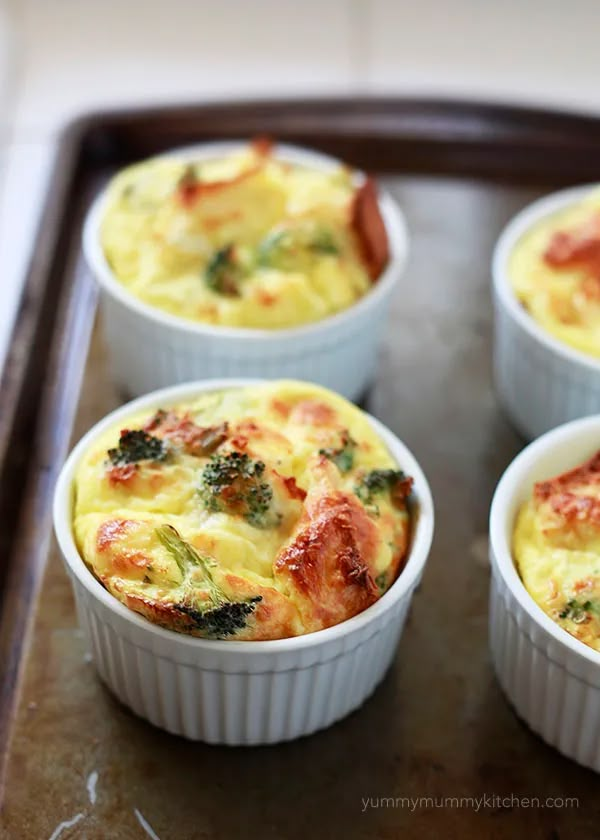 four small cups filled with food sitting on top of a pan covered in broccoli