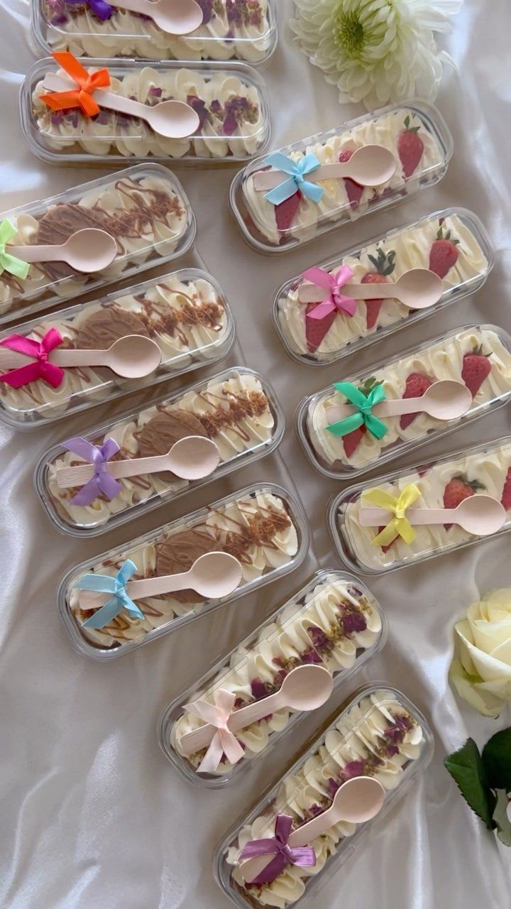 there are many desserts in plastic containers with spoons and flowers on the table