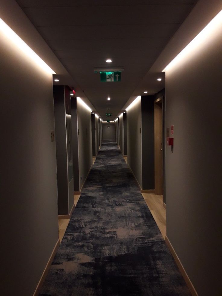 an empty hallway with lights on either side and carpeted flooring down the middle