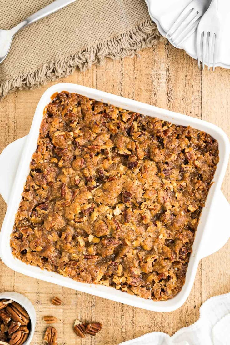 a casserole dish filled with granola and pecans on a wooden table