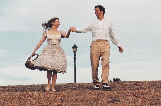 a man and woman are holding hands while walking in the grass near a street light