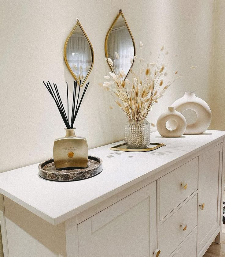 a white dresser topped with vases filled with flowers and reeds on top of it