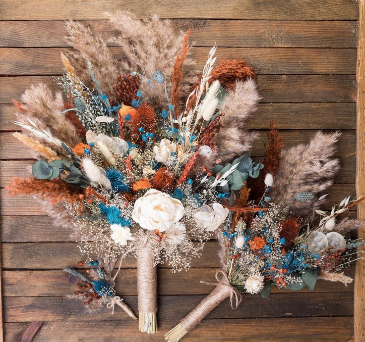 an arrangement of dried flowers and feathers on a wooden background