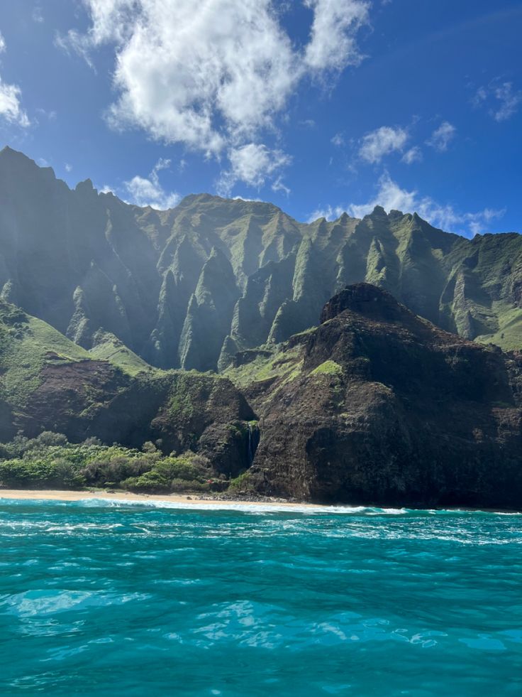 an island with mountains in the background under a blue sky and some clouds above it