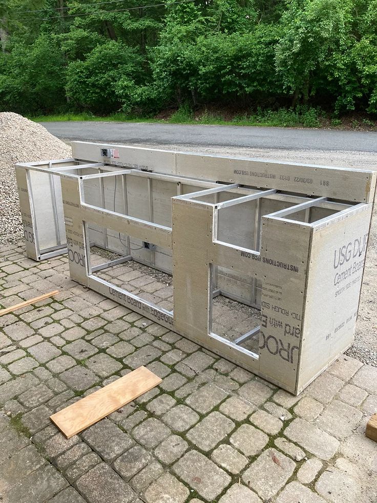 an outdoor kitchen made out of concrete sitting on the side of a road in front of some trees