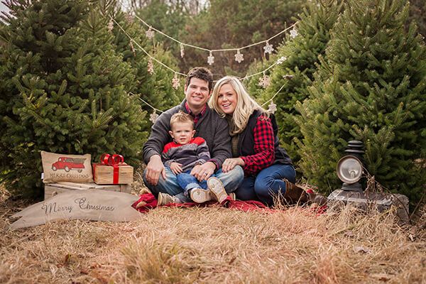 a man and woman sitting in front of christmas trees with a baby on their lap