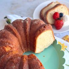 a bundt cake on a plate next to a bowl of strawberries and a piece of bread