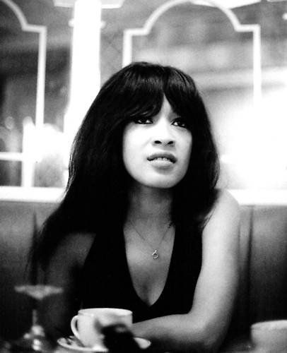 a black and white photo of a woman sitting at a table with a cup in front of her