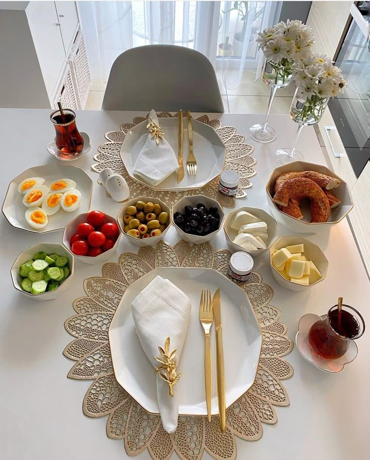 a white table topped with lots of plates and bowls filled with food next to flowers