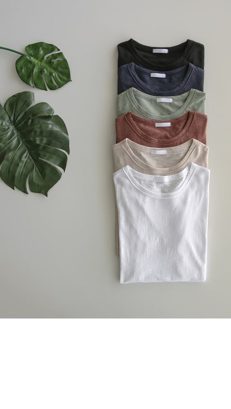 five t - shirts sitting on top of a table next to a plant