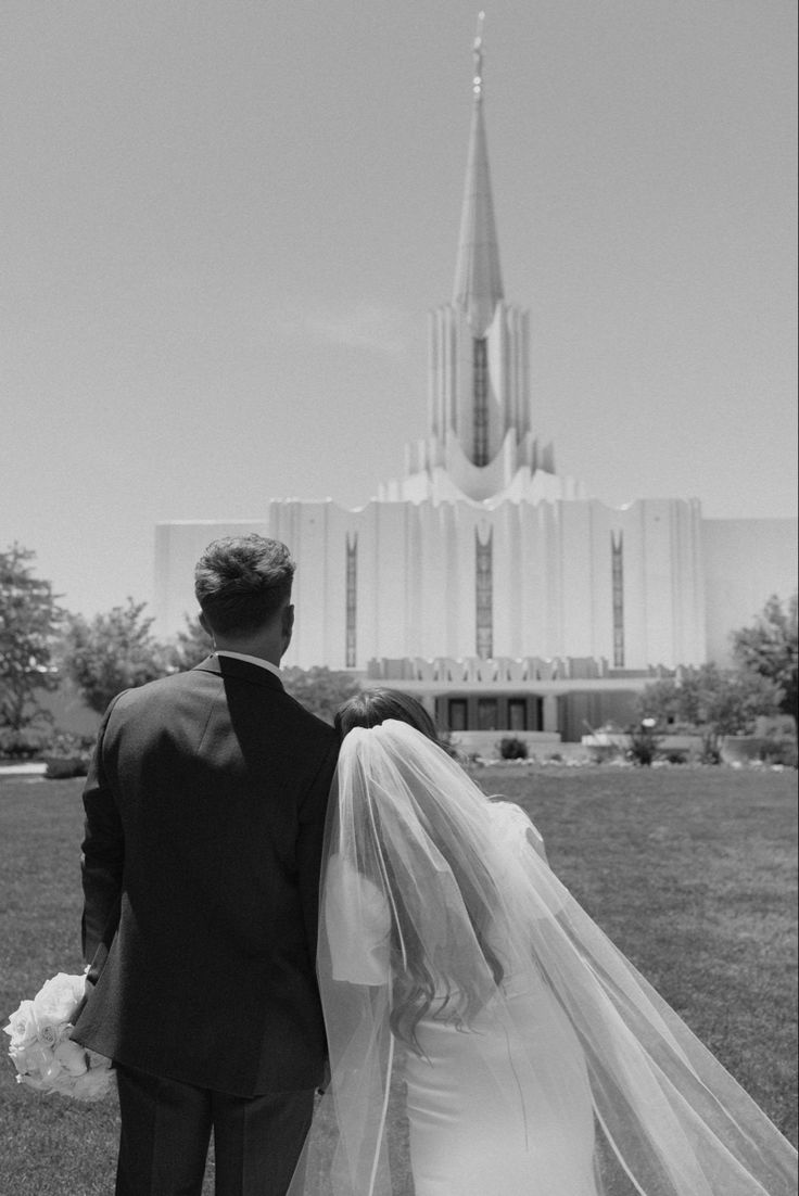 a bride and groom walking towards the mormon temple on their wedding day in black and white