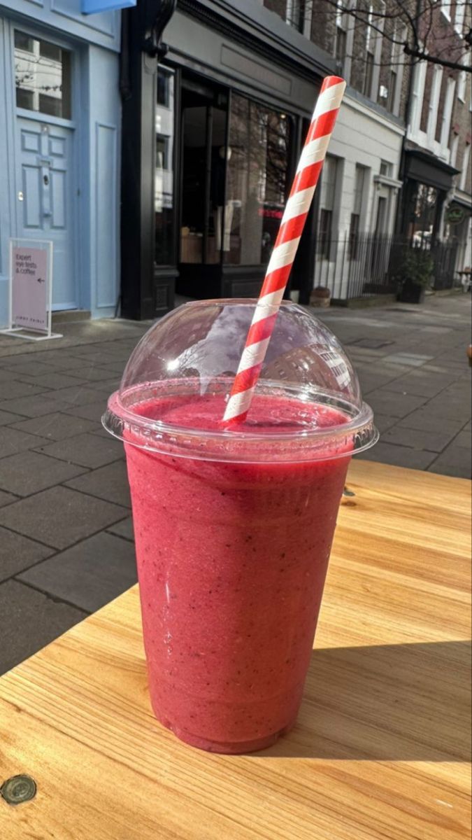 a smoothie in a plastic cup with a striped straw sitting on a wooden table