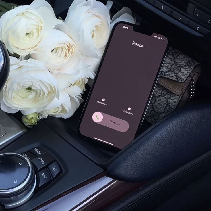 an iphone is sitting on the dashboard of a car next to flowers and a clock