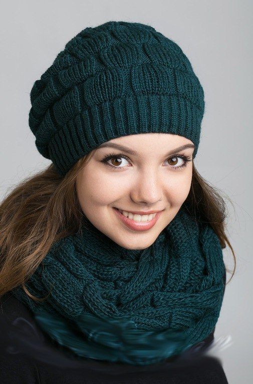 a woman wearing a green knitted hat and scarf smiles at the camera with her long hair in front of her face