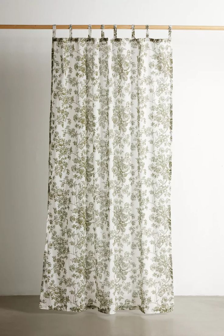 a curtain hanging on a wooden rod in front of a white wall with green flowers