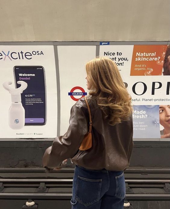 a woman standing in front of a sign with an advertisement on the wall behind her