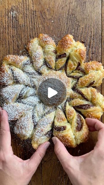 two hands holding pastries in front of a wooden table with powdered sugar on top