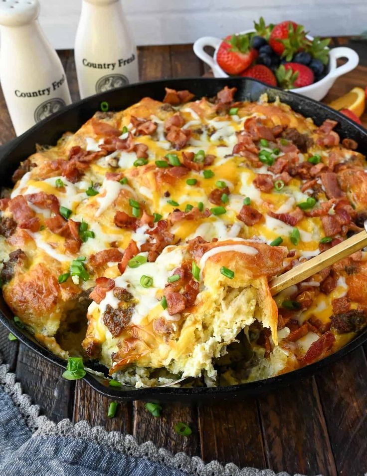 a breakfast casserole with bacon, cheese and green onions in a cast iron skillet