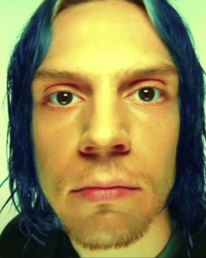 a man with blue hair is looking at the camera