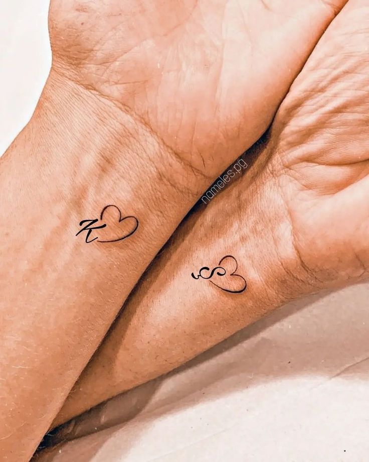 two people with matching tattoos on their wrists, one is holding the other's hand