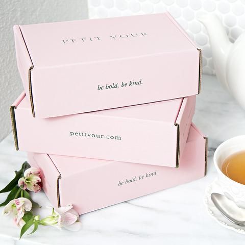 three pink boxes sitting on top of a table next to a cup and saucer