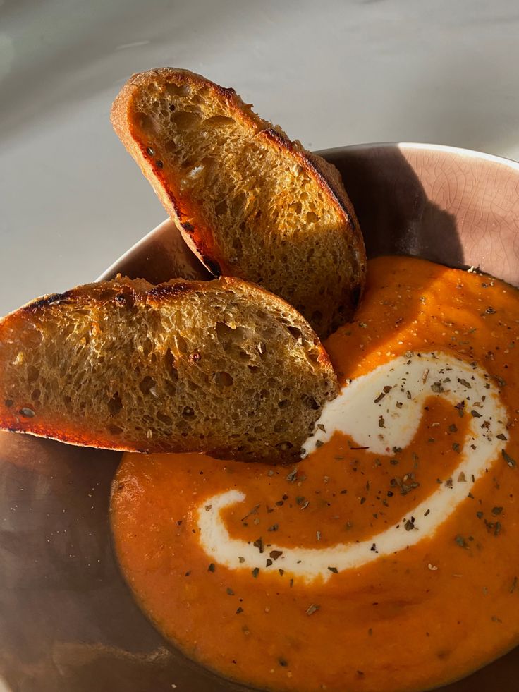 two pieces of bread sticking out of a bowl of tomato soup with cream in it