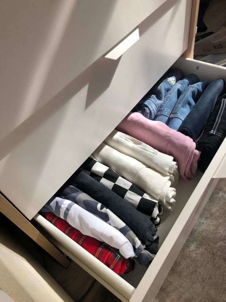 an open drawer filled with clothes on top of a carpeted floor next to a wall