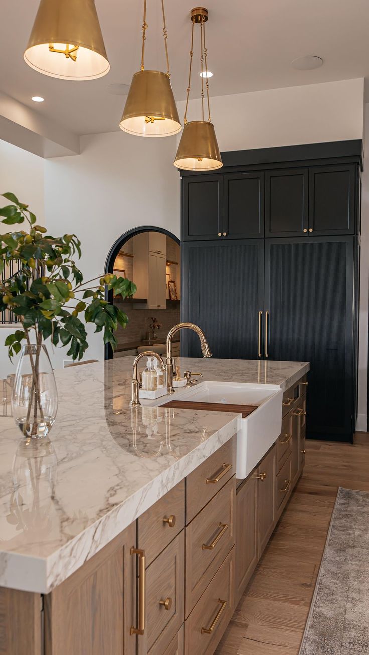 a kitchen with marble counter tops and gold pendant lights hanging from the ceiling over the sink