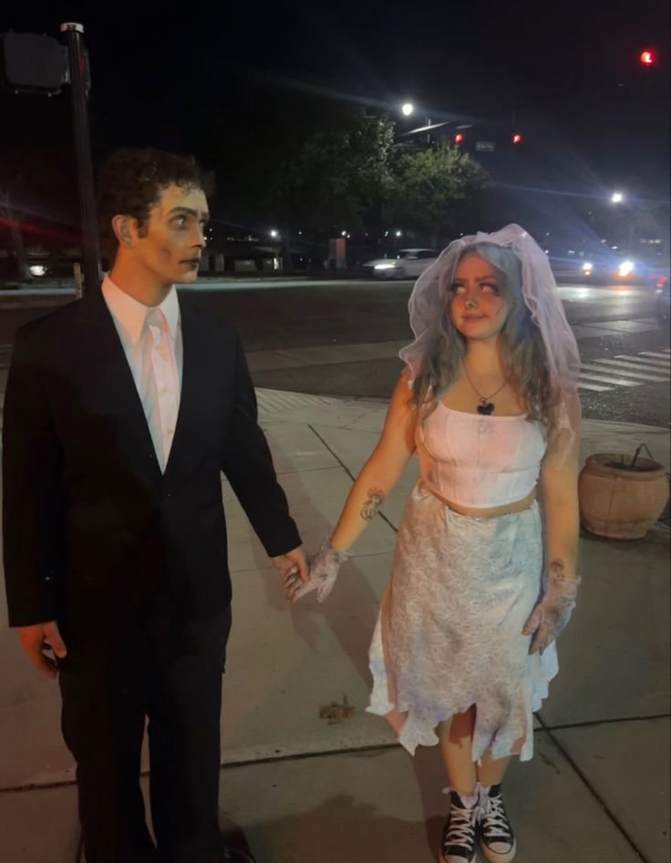 a man and woman dressed up as bride and groom holding hands on the sidewalk at night