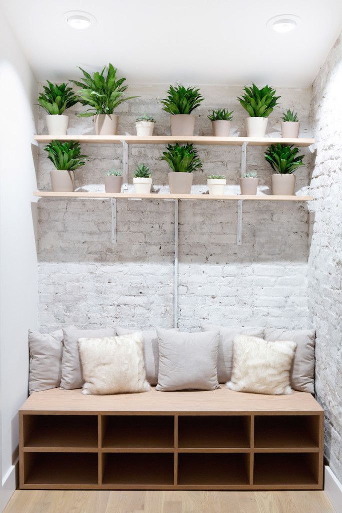 a white brick wall with shelves and plants on it's sides, in front of a wooden bench