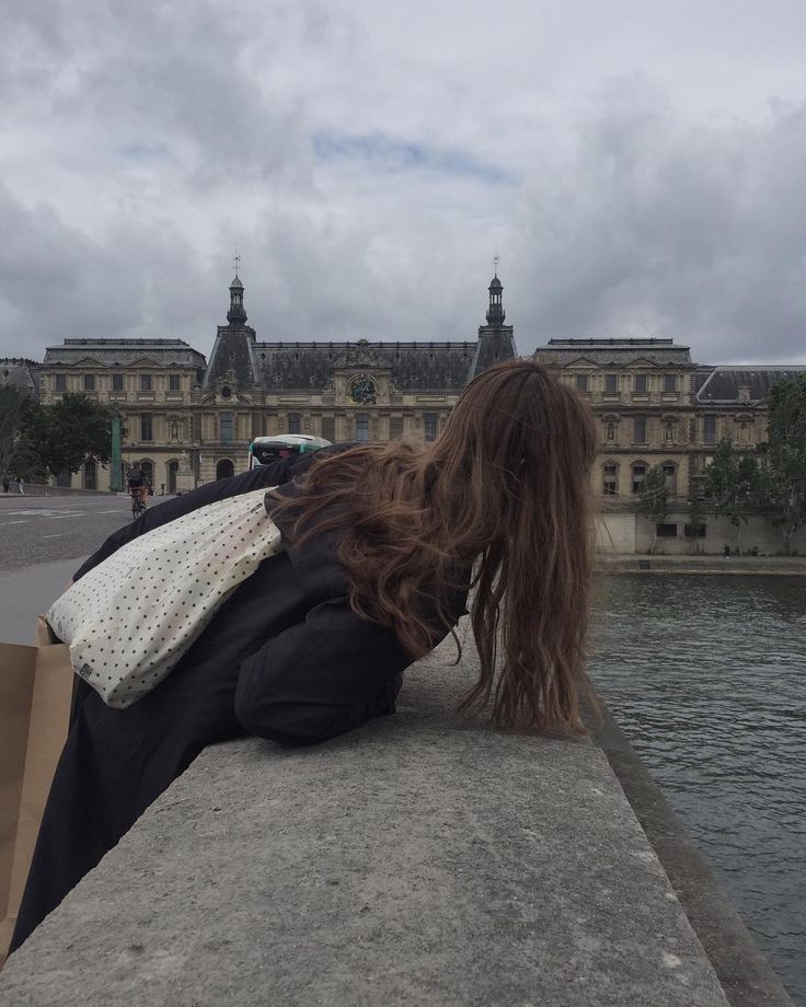 a woman with long hair laying on the edge of a wall next to a body of water