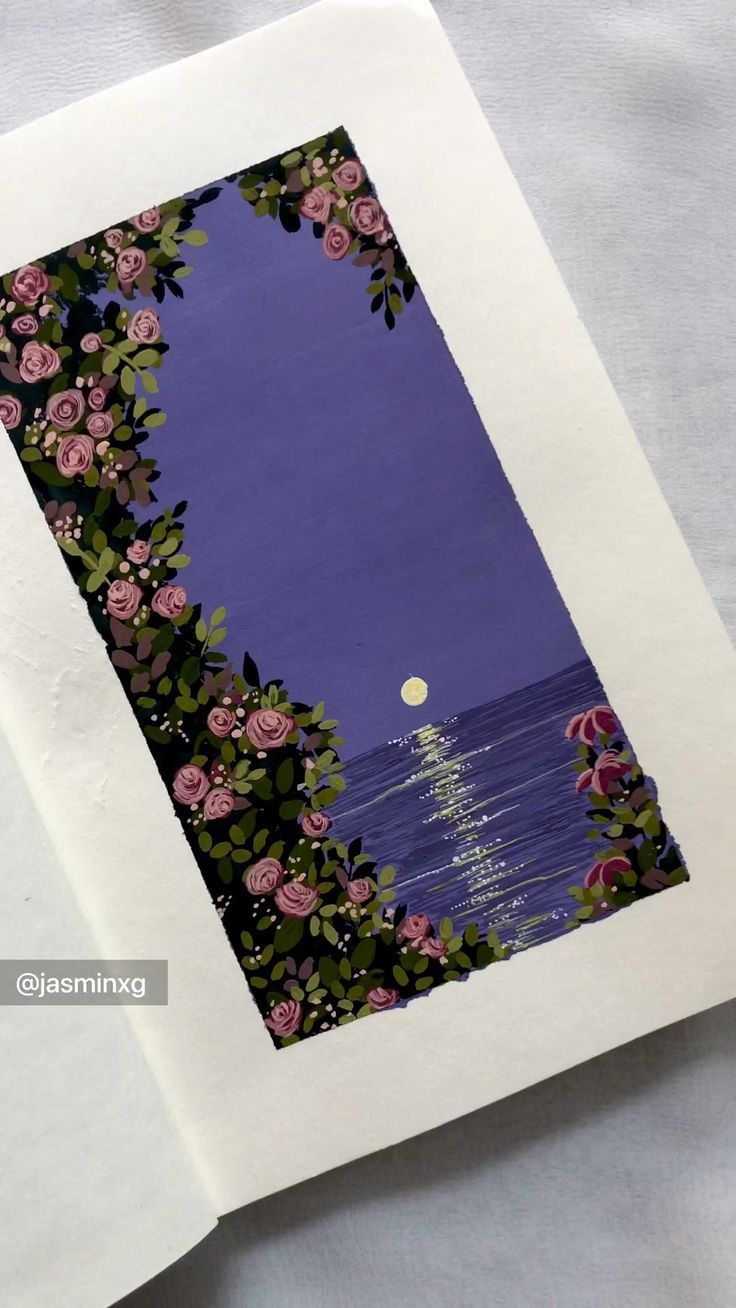 an open book with pink flowers on it and a full moon in the sky above water