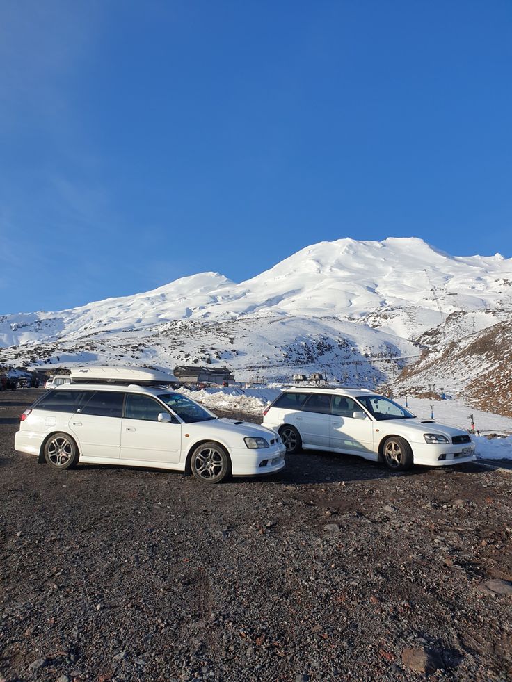 two white cars parked in front of a mountain