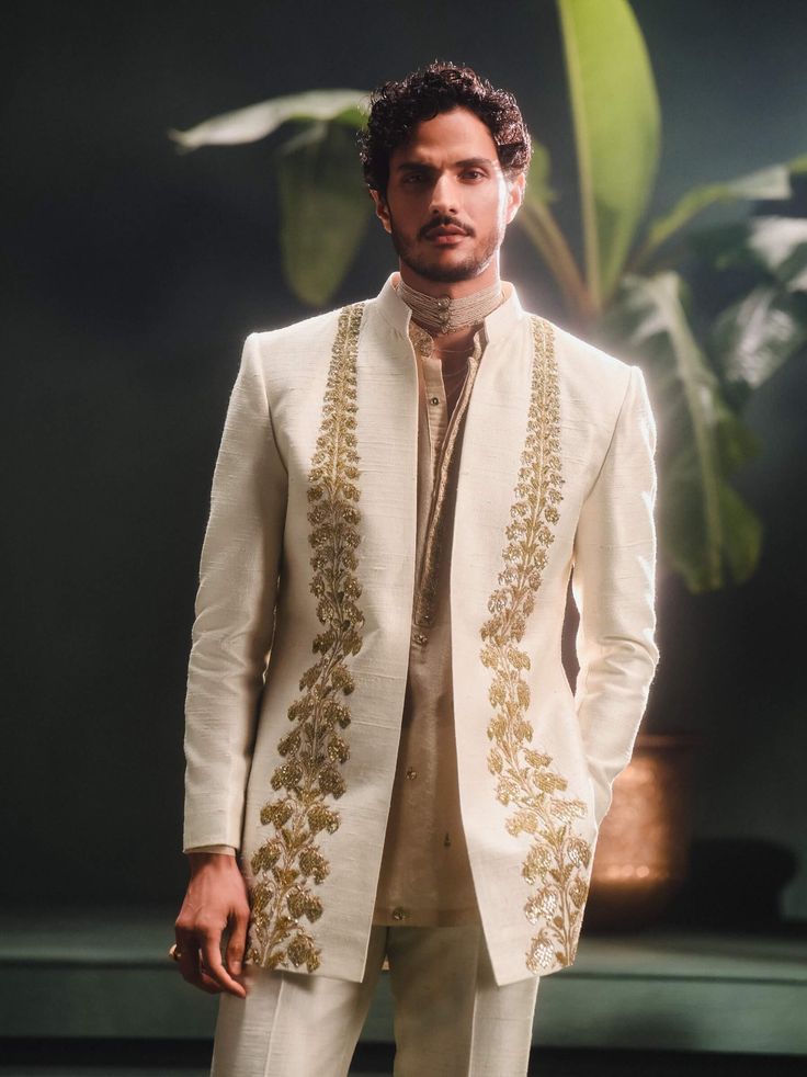 Step into refined elegance with the Kaju Katli Raja koti, an opulent sherwani adorned with intricate gold zardozi, katdana, and pearl embroidery, inspired by 'Berry Bel'. The ensemble includes a short georgette tissue kurta that adds a playful touch and straight, tailored pants for a smart finish. This piece is a perfect blend of grandeur and modern sophistication. Chanderi Bandhgala With Traditional Drape For Designer Wear, Traditional Drape Bandhgala In Chanderi For Eid, Festive Sherwani With Gota Work, Elegant Chanderi Bandhgala For Transitional Season, Festive Bandhgala With Gota Work For Eid, Elegant Chanderi Nehru Jacket With Traditional Drape, Elegant Nehru Jacket With Traditional Drape In Chanderi, Dola Silk Cutdana Kurta For Reception, Reception Dola Silk Kurta With Cutdana