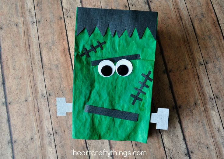 a paper bag with a green monster face and black eyes on the inside, sitting on a wooden floor